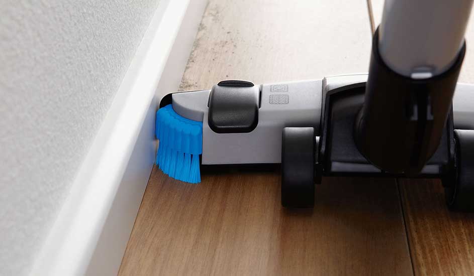 Een Philips stofzuigermond met blauwe borstel reinigt efficiënt langs de rand van een houten vloer.
