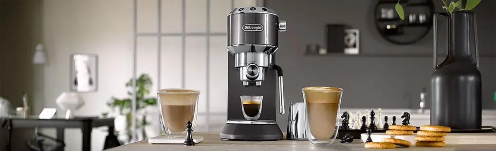 Op de afbeelding staat een De’Longhi espressomachine op een aanrecht, met twee glazen koffie en koekjes ernaast. Het merk is goed zichtbaar.