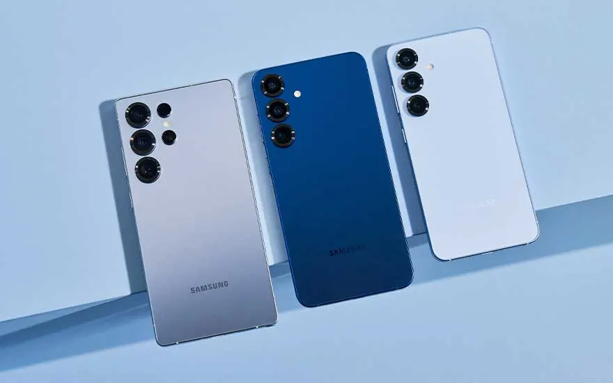 Drie Samsung-smartphones staan naast elkaar op lichtblauw decor en tonen hun achterzijde met meerdere cameralenzen in diverse kleuren.