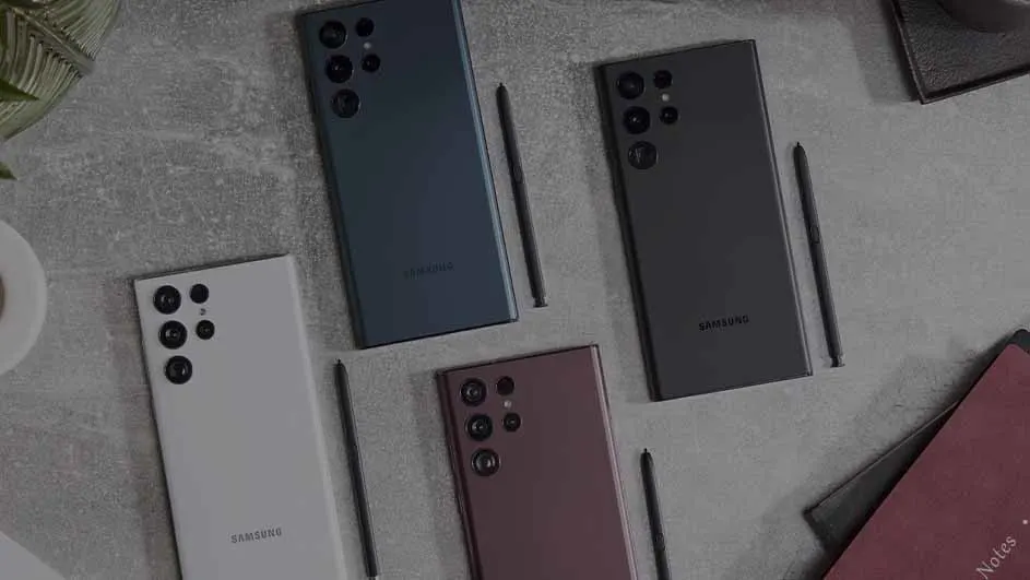 Vier Samsung telefoons en pennen liggen op een grijze ondergrond, met een plant, notitieboek en kopje in de hoeken.