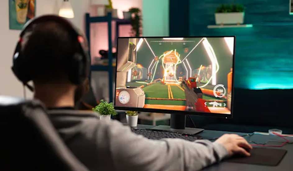 Gamer wearing headset sits at wide monitor, playing colourful sci-fi shooter, hand on mouse in warmly lit modern room.