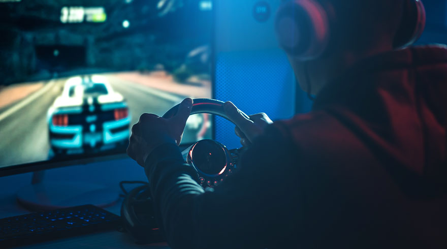 Een persoon speelt een racegame met een stuurwiel voor een scherm met een witte auto op een weg.