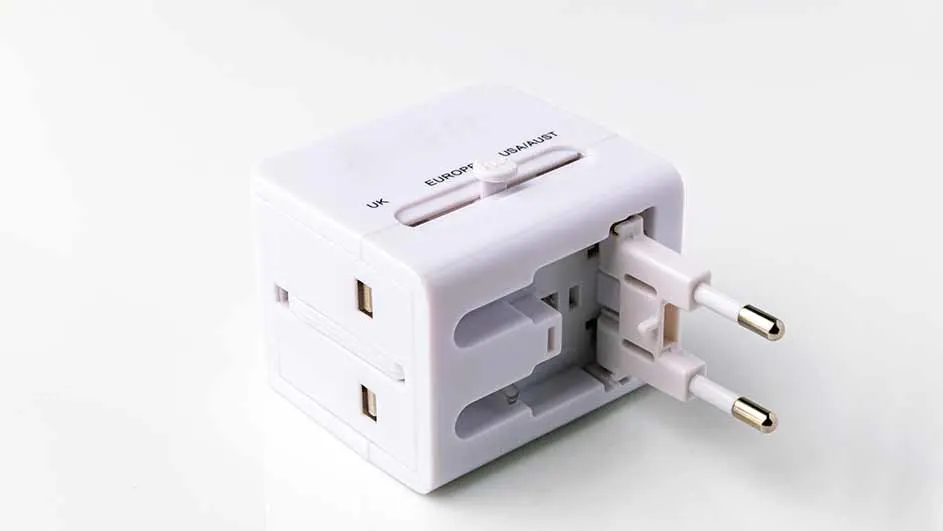 Een witte universele reisadapter met pinnen voor Europa steekt uit een zijde, op een witte ondergrond.