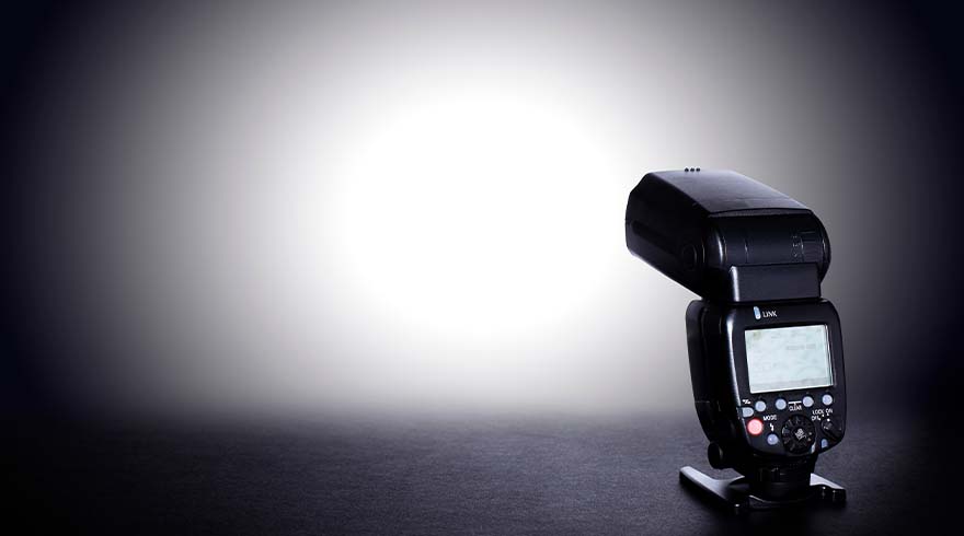 Een zwarte flitser staat op een tafel tegen een grijze achtergrond met een witte lichtvlek in het midden.