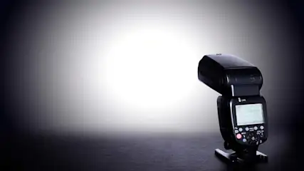 Een zwarte flitser staat op een tafel tegen een grijze achtergrond met een witte lichtvlek in het midden.