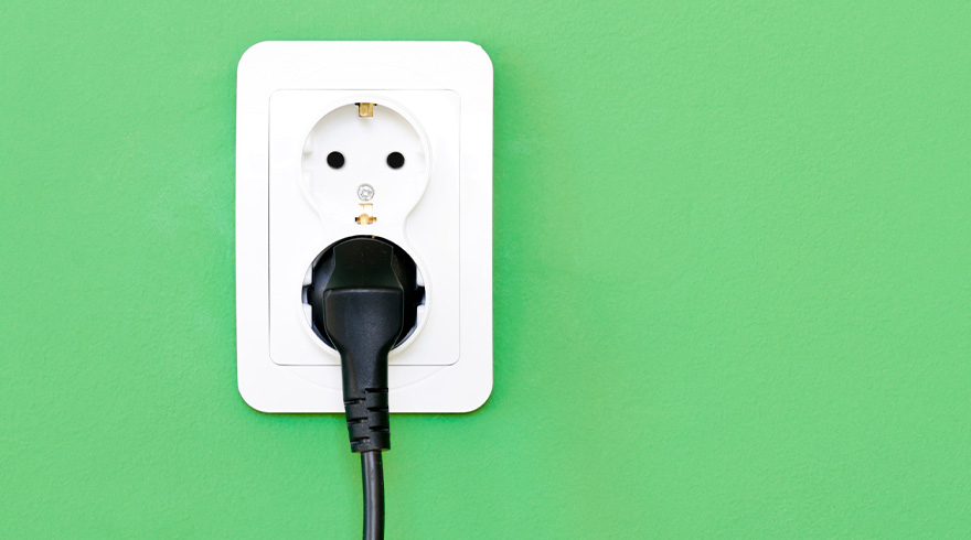 Een witte wandcontactdoos met een zwarte stekker tegen een groene achtergrond.