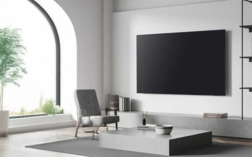 Minimalistische witte woonkamer met zwarte TV aan de muur, moderne fauteuil en groot boogvenster met groene planten.