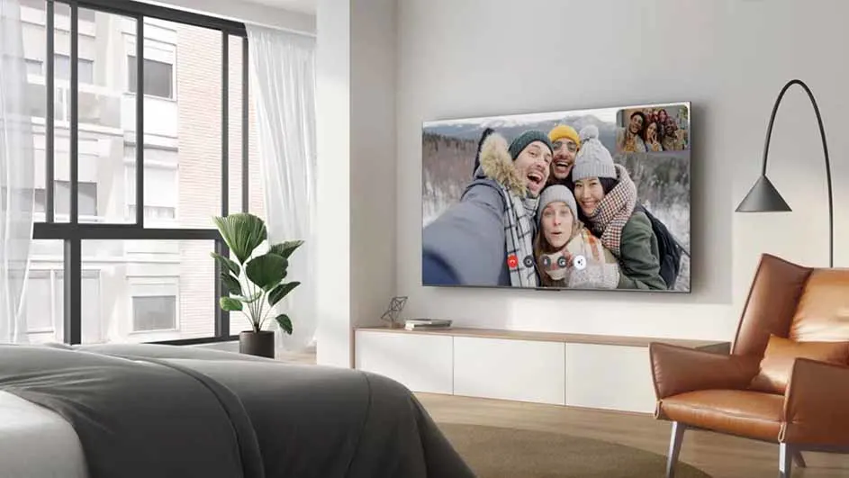 TCL-televisie gemonteerd aan de slaapkamerwand, toont een videogesprek met vier lachende mensen in winterkleding.