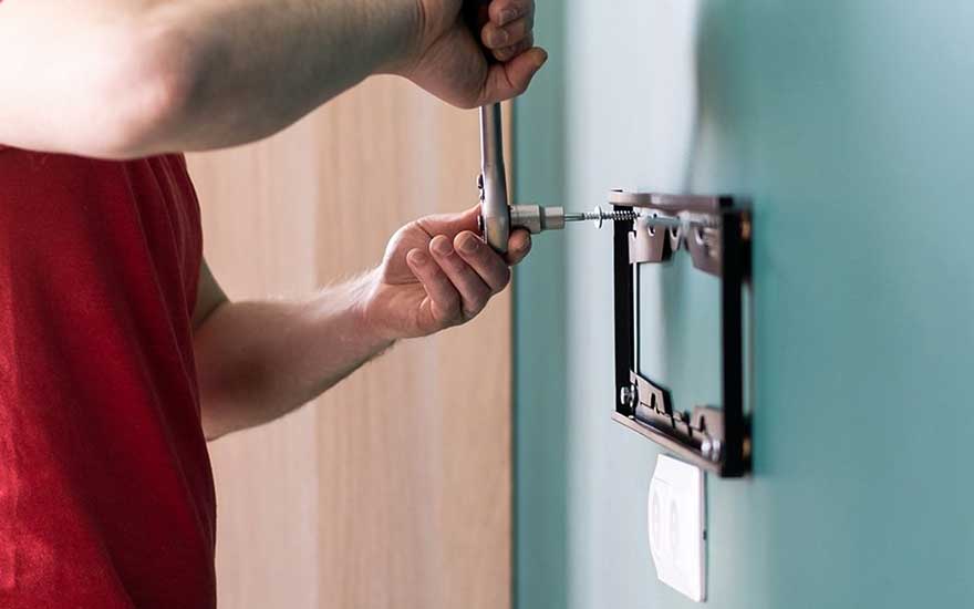 Close-up van iemand die een muurbeugel vastschroeft, vermoedelijk voor de installatie van een tv aan de muur in een huis.