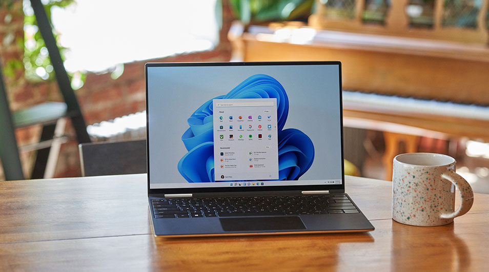 Laptop op tafel met Windows-scherm, mok ernaast. Achtergrond toont piano en bakstenen muur.