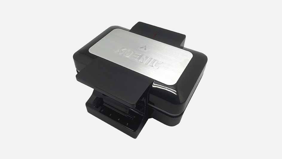 Een zwart wafelijzer met een zilveren plaat bovenop, tegen een effen witte achtergrond.