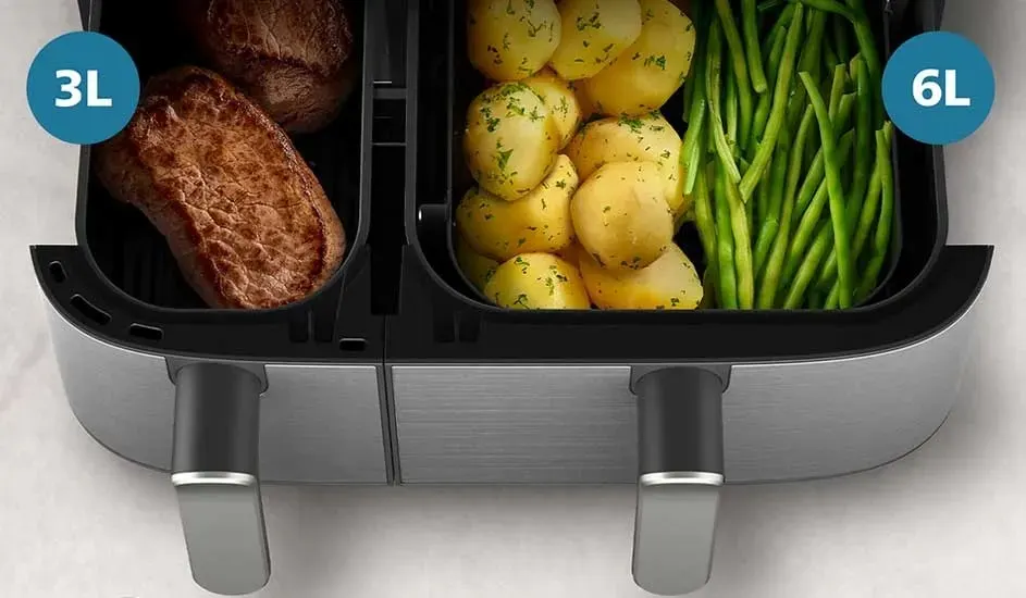In a Philips air fryer there are steaks in the left 3L drawer and potatoes with green beans in the right 6L drawer.