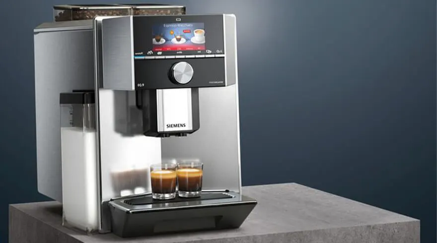 Een zilverkleurig Siemens koffiezetapparaat op een oppervlak met twee glazen espresso, tegen een blauwe achtergrond.