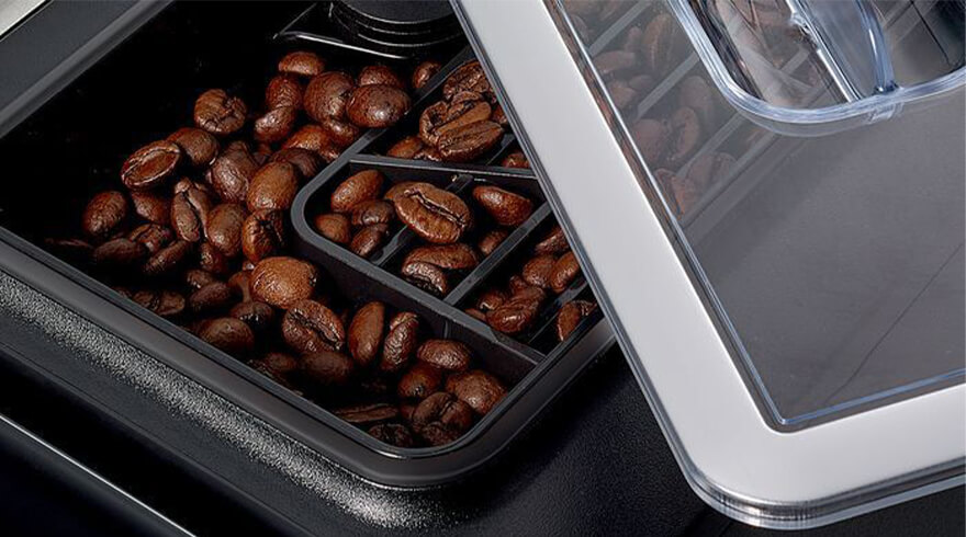 Koffiebonen in een zwart bakje met een doorzichtig deksel, in een machine.