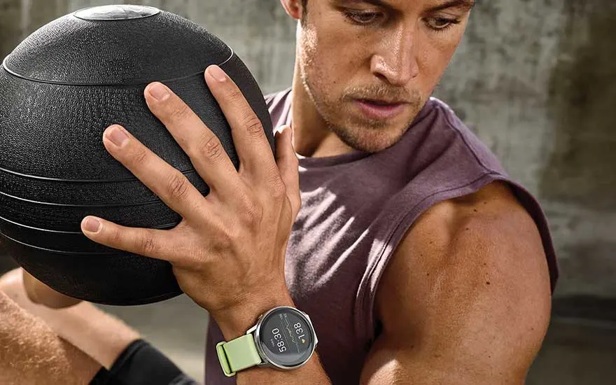 Een man traint met een fitnessbal, een groene Garmin smartwatch aan zijn pols, gefocust op zijn oefening.
