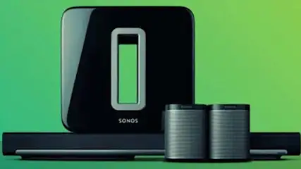 Zwarte Sonos subwoofer met twee grijze speakers en een zwarte soundbar tegen een groene achtergrond.