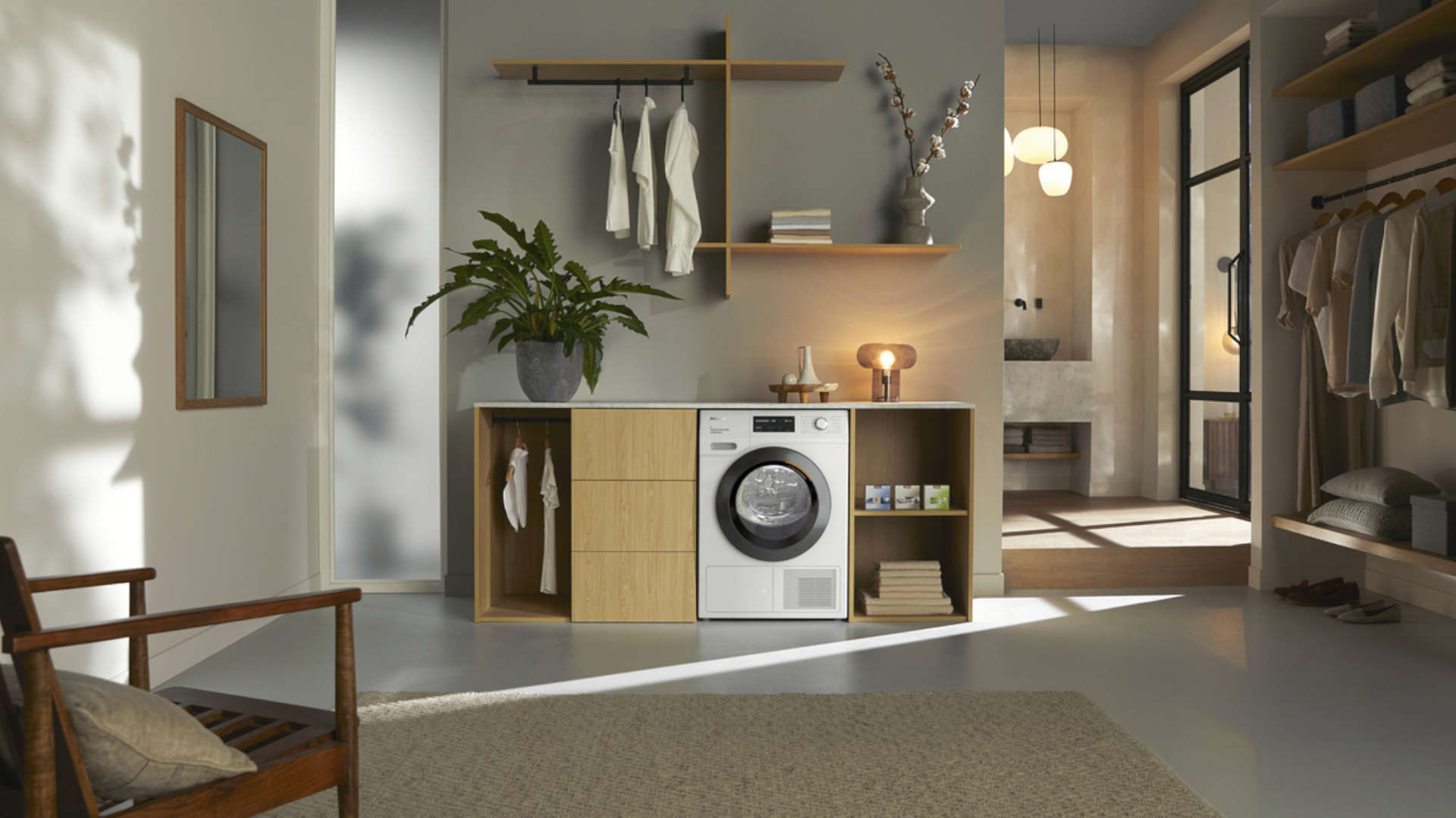 Woonkamer met wasmachine in kast, houten stoel, spiegel aan de wand, plant en open kast met kleding.