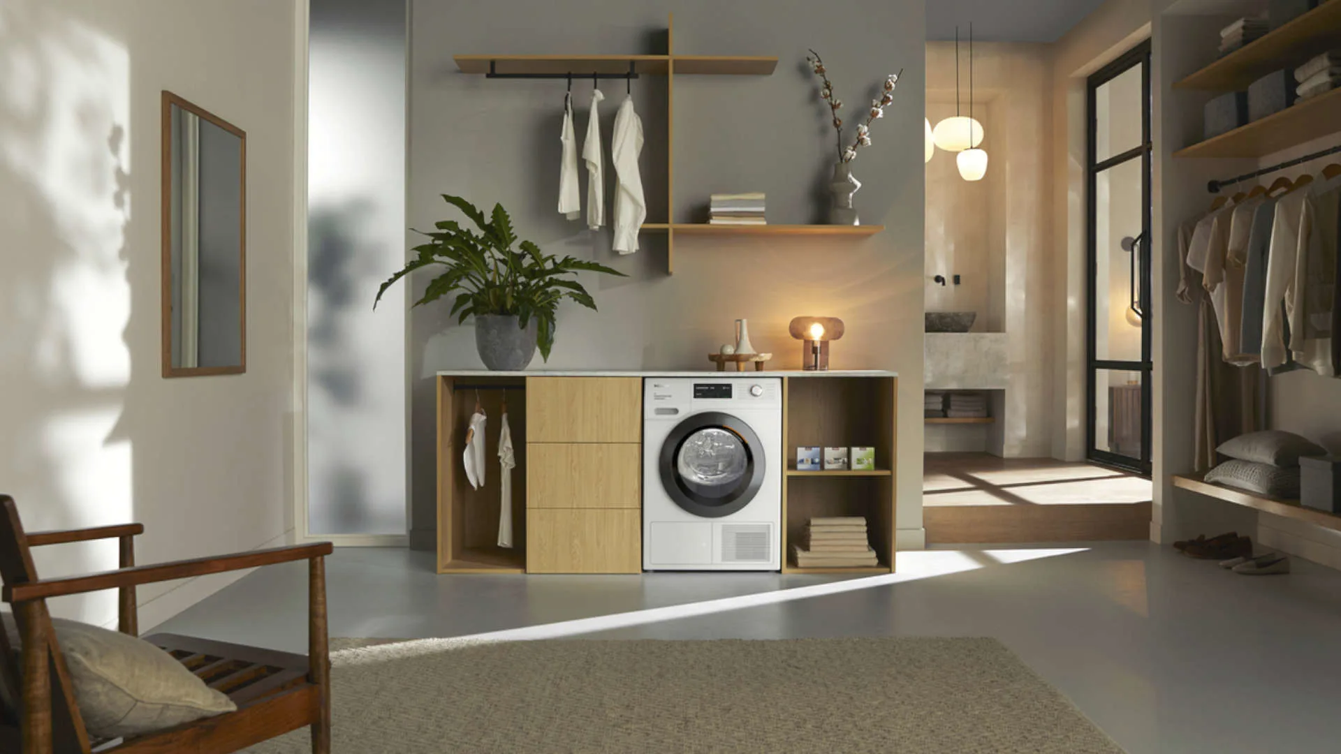 Woonkamer met wasmachine in kast, houten stoel, spiegel aan de wand, plant en open kast met kleding.