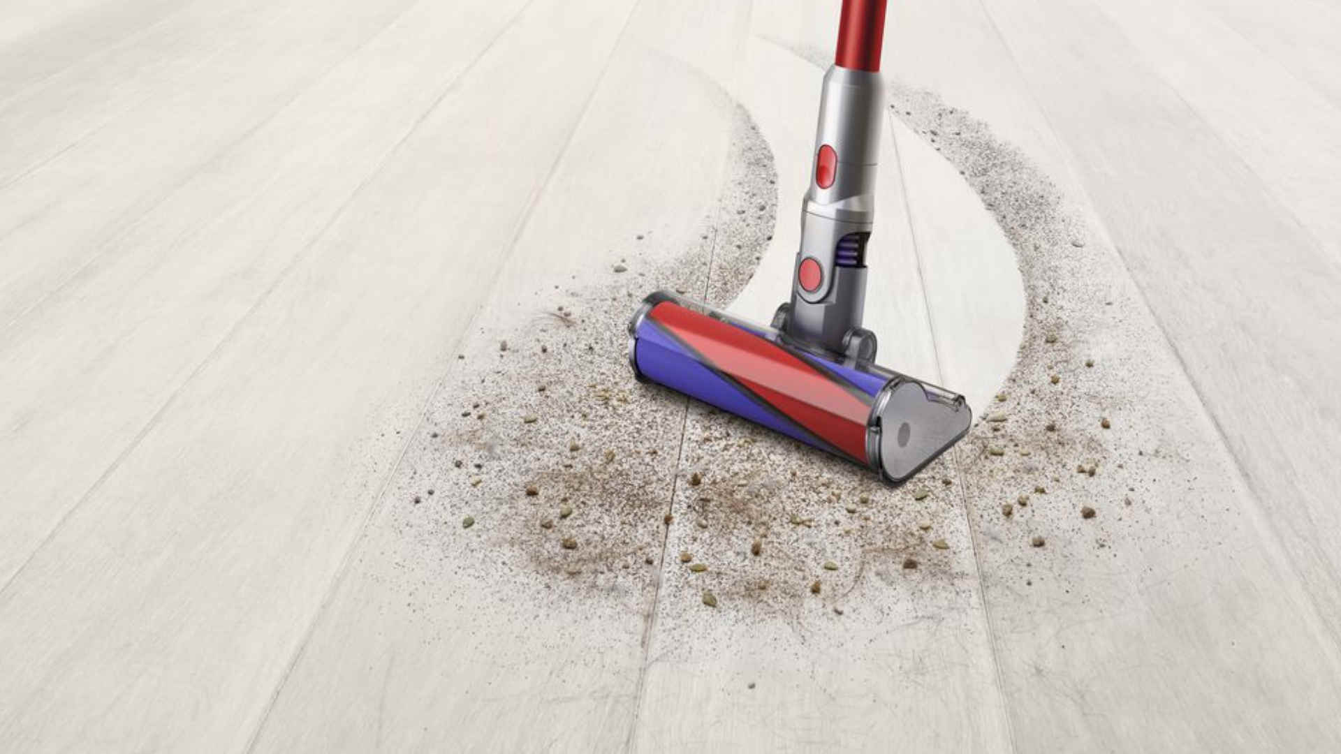 Een rode en blauwe stofzuiger maakt een houten vloer schoon, er is vuil te zien.