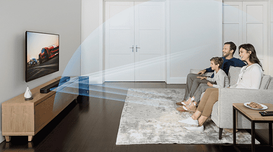 Een familie zit op een grijze bank voor een tv-scherm in een woonkamer met een grijze vloerkleed.