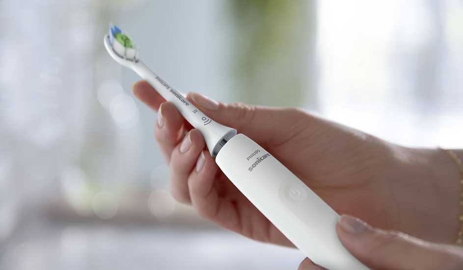 Een hand houdt een witte Philips Sonicare elektrische tandenborstel vast. Het ontwerp is slank, modern en ergonomisch, met een duidelijke aan-knop.