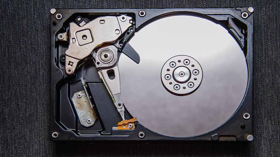 Een geopende harde schijf met een zilverkleurige schijf en metalen onderdelen op een donkere achtergrond.