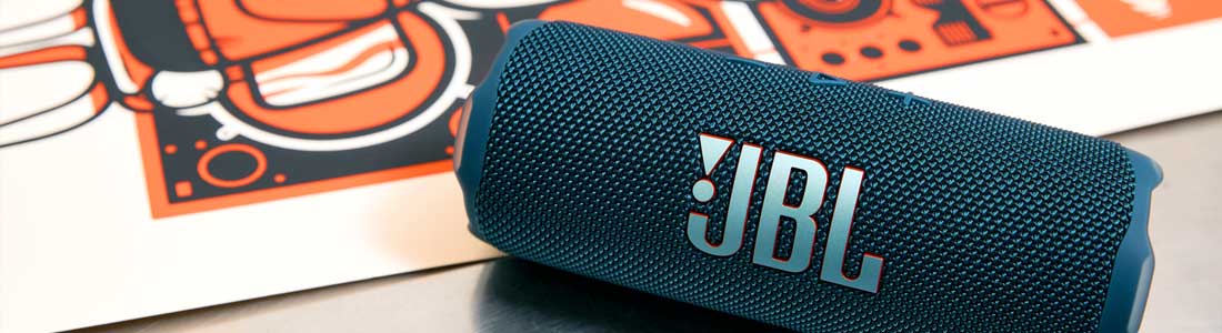 Blue JBL Bluetooth speaker lying at an angle on a table with a colorful poster in the background.