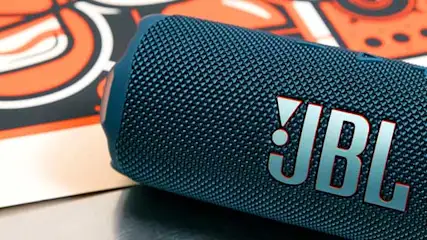 Blue JBL Bluetooth speaker lying at an angle on a table with a colorful poster in the background.