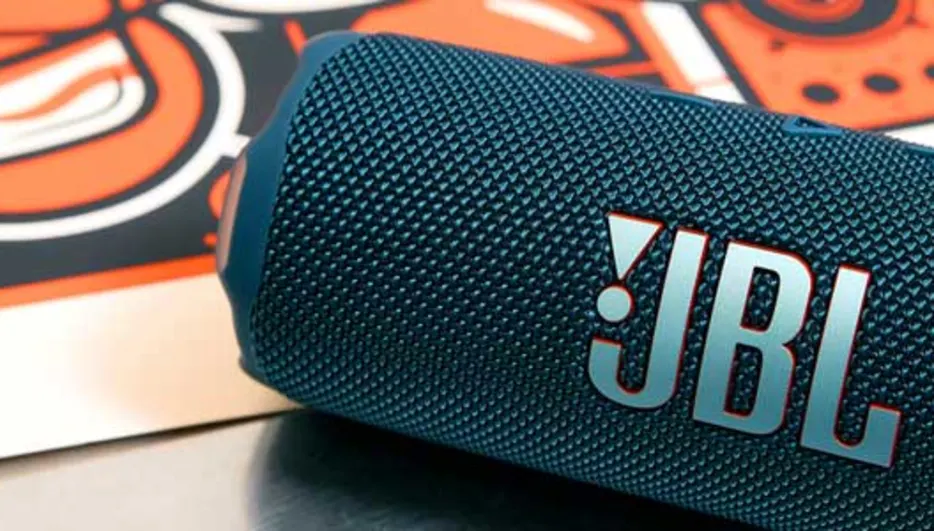 Blue JBL Bluetooth speaker lying at an angle on a table with a colorful poster in the background.