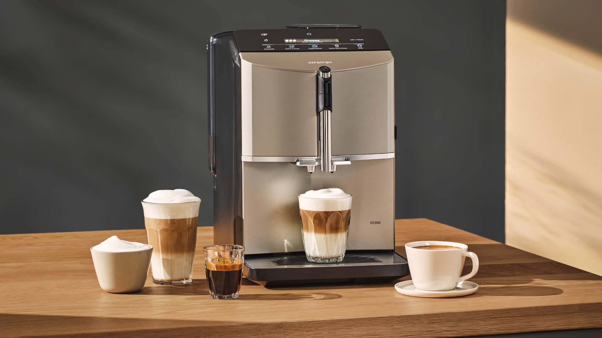 Koffiemachine met kopjes koffie en espresso op een houten tafel. Achtergrond is donkergrijs.
