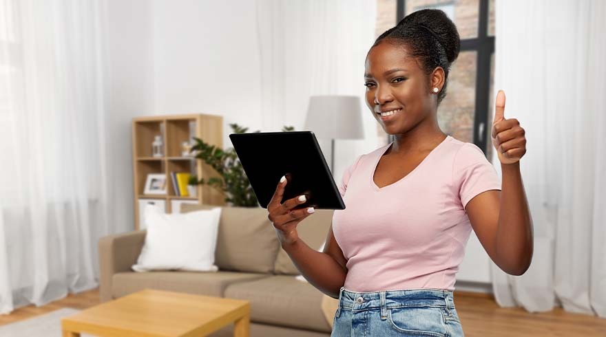 Vrouw met tablet in woonkamer, duim omhoog. Achtergrond: bank, kast, lamp, raam met gordijnen.