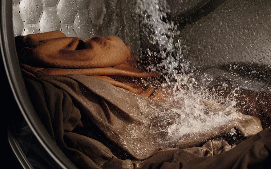 Close-up van wasmachine trommel met water dat over bruine kleding stroomt tijdens het spoelproces. 