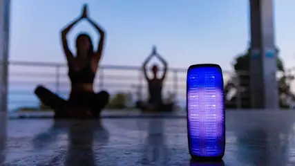 Een blauwe luidspreker staat voor twee mensen die yoga doen in kleermakerszit met hun armen omhoog.