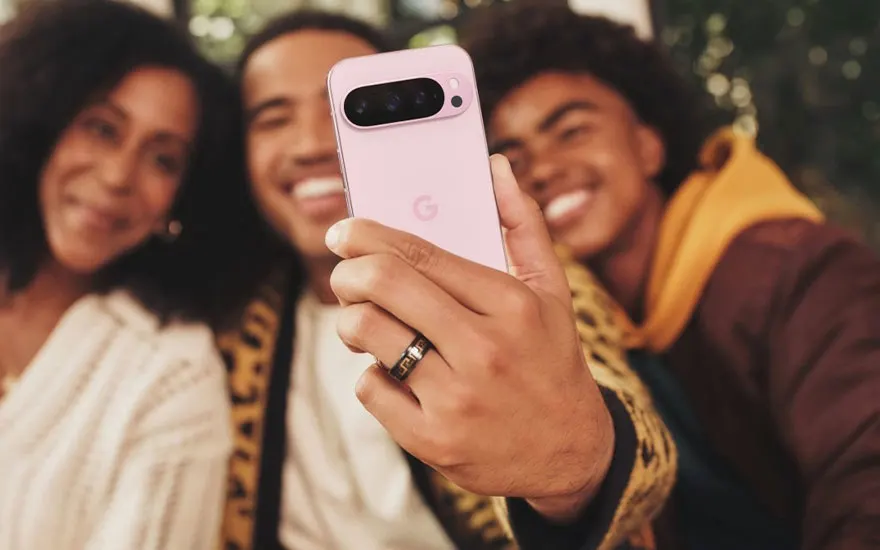 Drie vrienden maken een selfie met een roze Google Pixel smartphone, allemaal glimlachend in een buitenomgeving.
