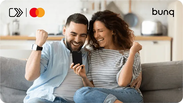 Blij koppel juicht op de bank met telefoon; logo’s van Mastercard en bunq in beeld.