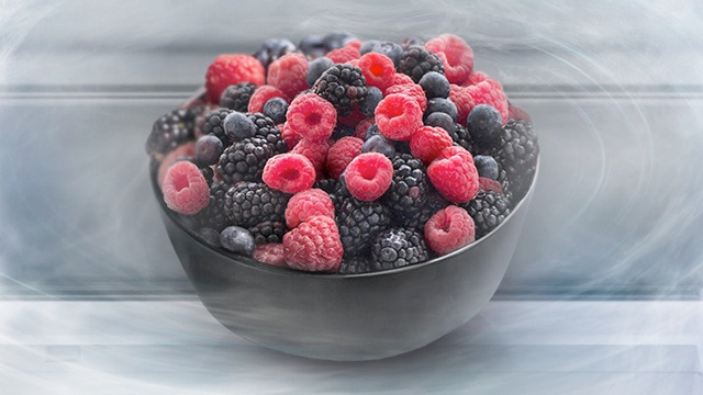 Een kom vol bramen, frambozen en bosbessen tegen een zachte, lichtblauwe achtergrond.