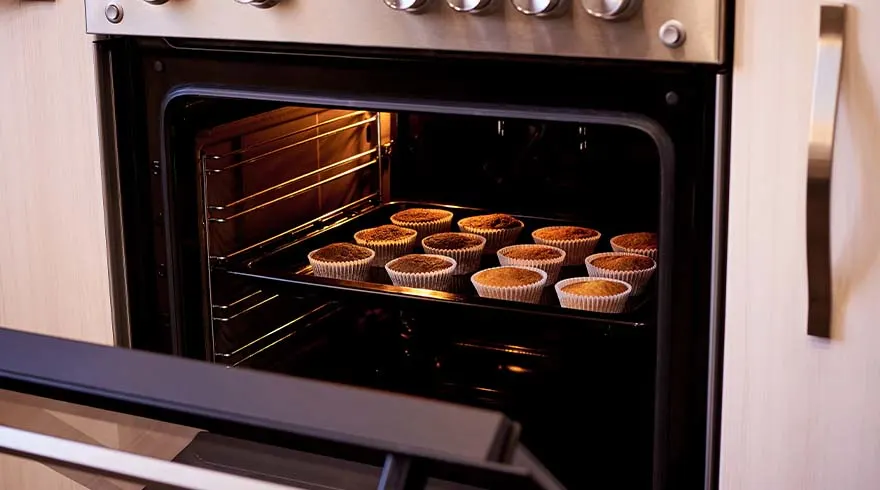 Een openstaande oven met een bakplaat vol muffins in papieren vormpjes.