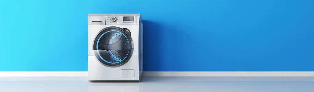 A washing machine is positioned against a blue wall with a white baseboard.
