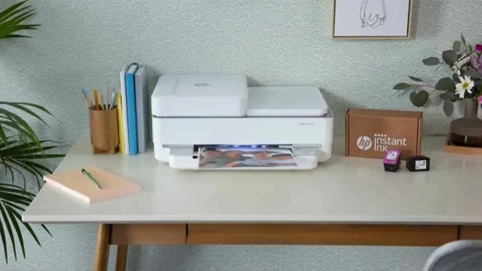 Een HP printer staat op een bureau met boeken, potloden, een doos HP Instant Ink en bloemen in een vaas ernaast.