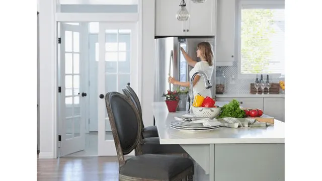 Een keuken met een vrouw die de koelkast opent. Op het aanrecht staan groenten en borden. Er staan twee stoelen aan het aanrecht.
