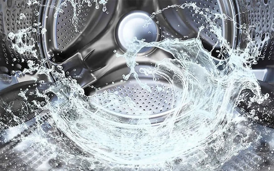 Water splashes inside a shiny, empty Samsung washing machine drum, highlighting the clean and modern stainless steel interior.