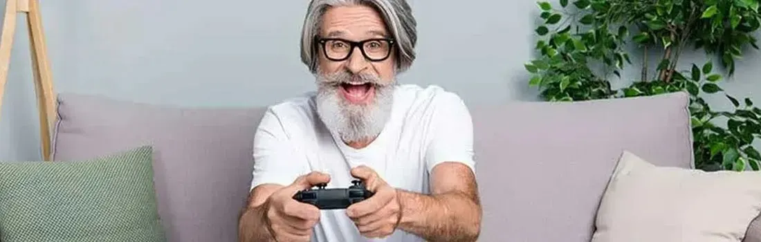Oudere man met bril en wit t-shirt zit op een paarse bank met een zwarte controller in zijn handen.