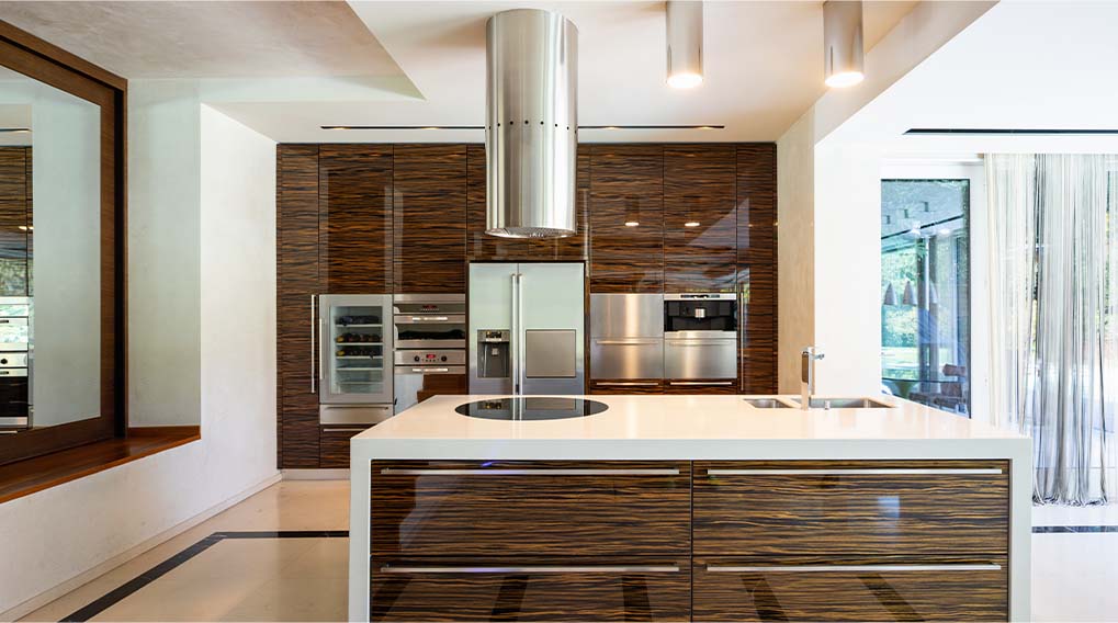 Een keuken met houten kasten, een wit eiland, roestvrijstalen apparaten en een moderne afzuigkap. Er is een raam met witte gordijnen.