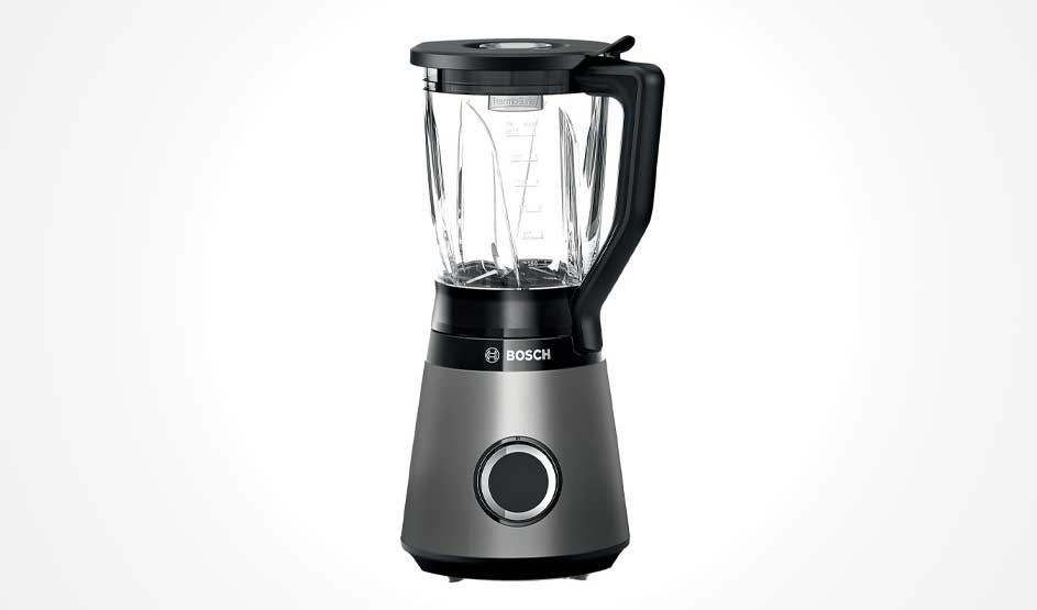 Een Bosch-blender staat op een witte achtergrond: glazen kan met zwarte deksel en handgreep, grijze voet met grote ronde draaiknop.