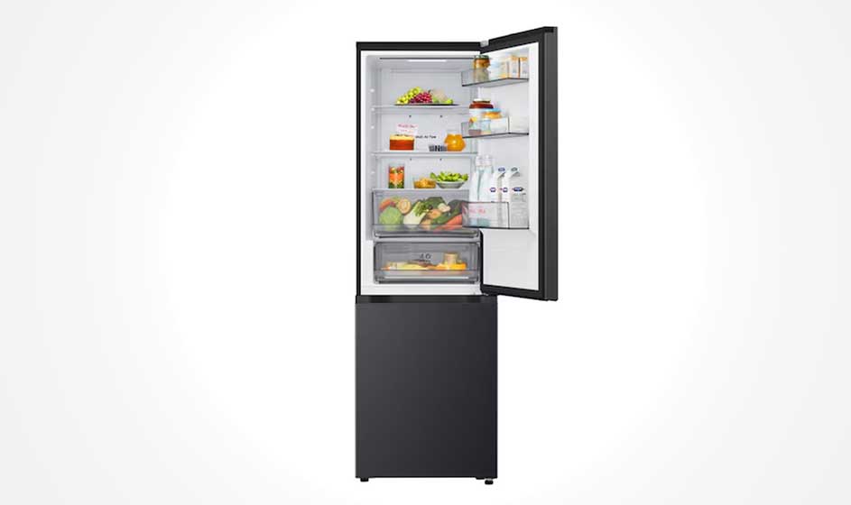 A black fridge freezer stands open, with food on glass shelves, bottles in the door and a lower freezer drawer against a white background.