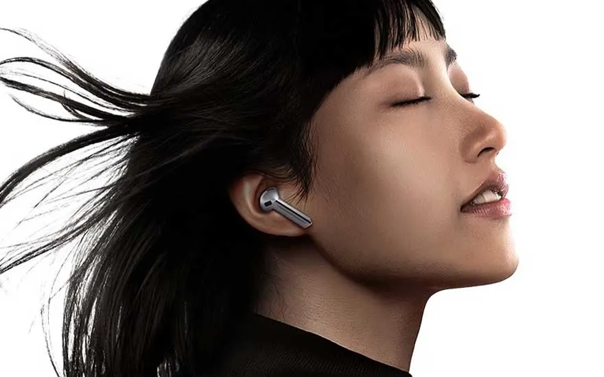 Vrouw met draadloze oortjes tient haar hoofd achterover, ogen gesloten, haar in beweging voor een heldere achtergrond.