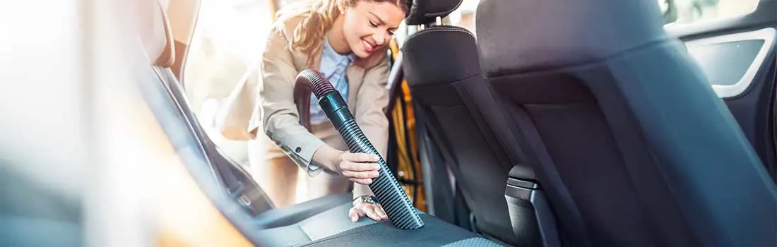 A woman is attentively vacuuming the inside of her car, focusing on cleaning the back seat to keep everything tidy and spotless.