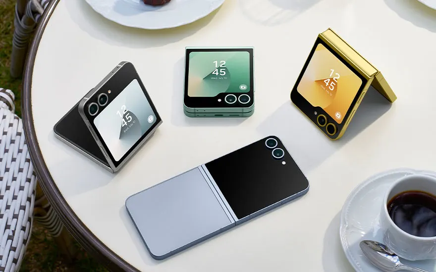 Vijf Samsung Galaxy Z Flip smartphones in verschillende kleuren op witte tafel met koffiekop en bord, sommige opgevouwen, andere gesloten.