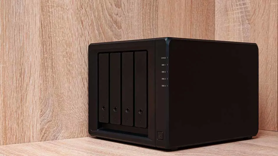 Een zwarte NAS-server met vier schijven staat tegen een houten wand.