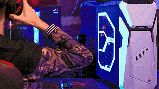 Een persoon met een koptelefoon zit voor een computer met een blauw verlichte kast en een scherm.